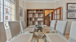 Ein modernes Wohnzimmer mit einem Glastisch, grauen Polsterstühlen, einem Holzregal und einem gerahmten Bild an der Wand.