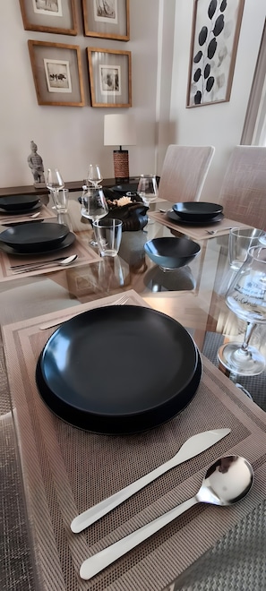 A dining table set with black plates, clear glasses, and silverware, framed by a decorative wall with framed artwork.