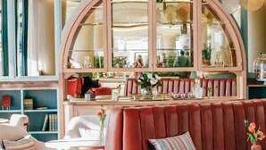 A seating area with a red upholstered bench, a white armchair, and a round table with a vase of flowers. - Elite Skyline Suite, Ellipse, Waterfall City (Midrand)