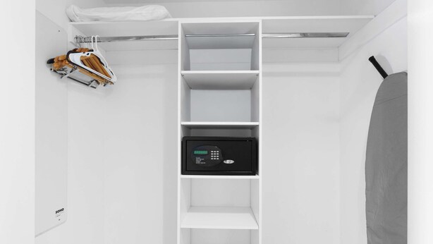A white closet with multiple shelves, a hanging rack, and a digital device on the middle shelf. - Elevated Living - 2BR - Intracoastal Views (Hallandale Beach)