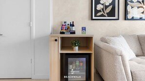 A modern living room with a wooden shelf holding snacks and drinks, a small potted plant, and a framed artwork on the wall. - Elevated Living - 2BR - Intracoastal Views (Hallandale Beach)