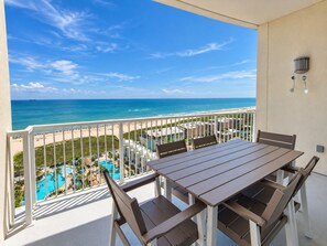 A balcony with a table and chairs overlooking a beach and pool area. - Sapphire 1605 - By GISO Vacation Rentals (South Padre Island)