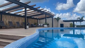 Ein moderner Außenpoolbereich mit Holzterrasse, Liegestühlen und einer Pergola.