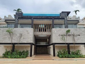 Ein modernes Gebäude mit einem zentralen Eingang, Balkonen und einem Schild mit der Aufschrift 'Cacao Tulum'.