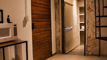 Ein Zimmer mit Holztür, Mikrowelle in Weiß, kleinem Tisch mit Sitzfläche aus Gewebe und Steinwand.