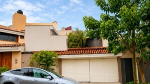 A modern building with a garage, a parked car, and a tree in the foreground. - Bowra Orquideas (Zapopan)