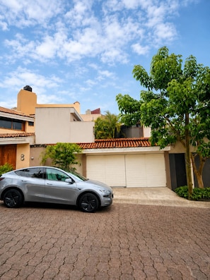 A modern building with a garage, a parked car, and a tree in the foreground.