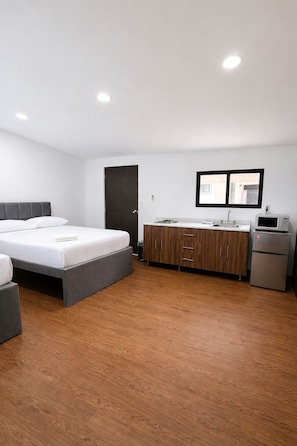 A modern bedroom with a bed, a small kitchenette, and a wooden floor.