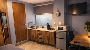 A compact room with a bed, kitchenette, and a desk with a chair.