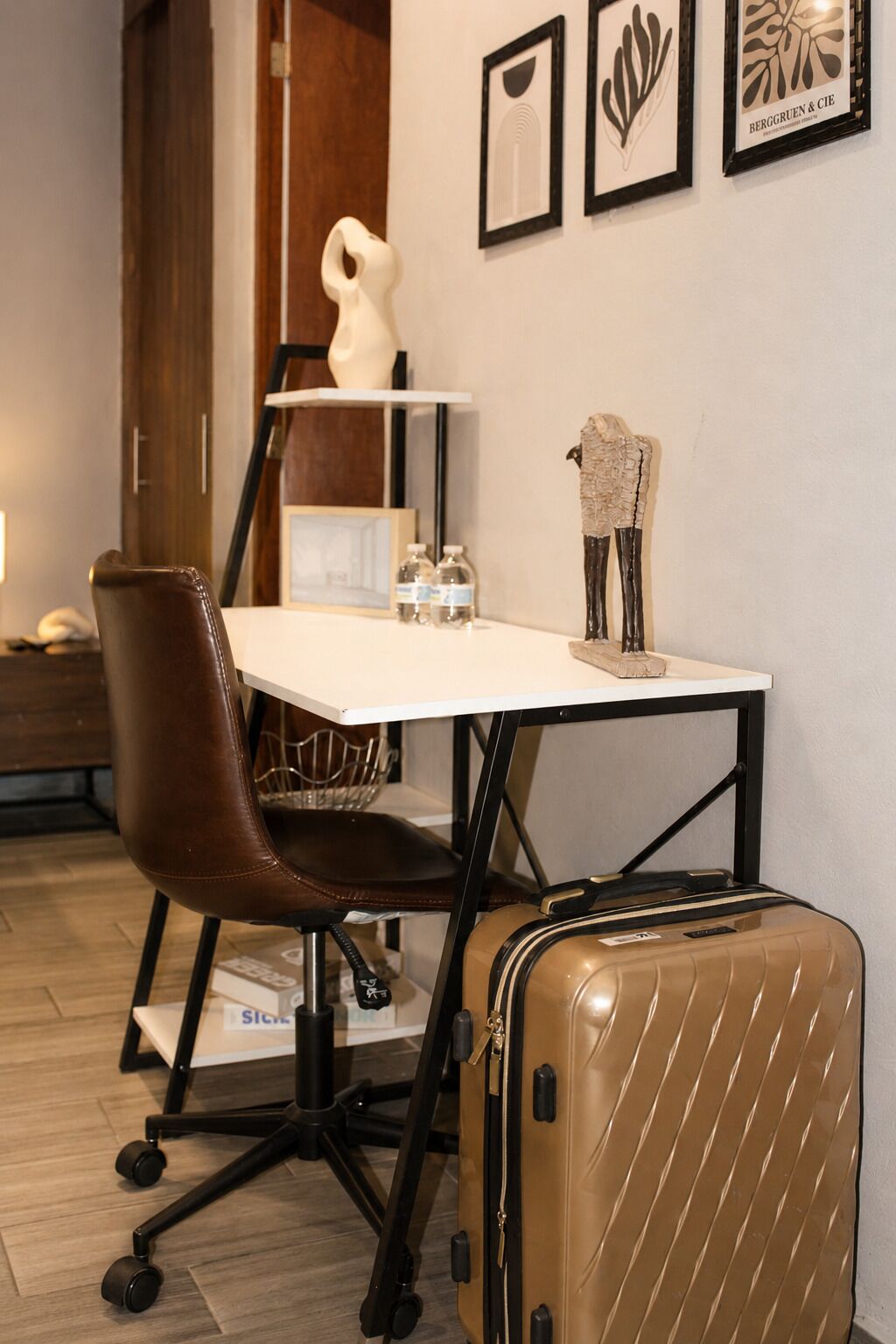 Habitación de hotel con escritorio, una silla de cuero marrón, una maleta y cuadros en la pared.