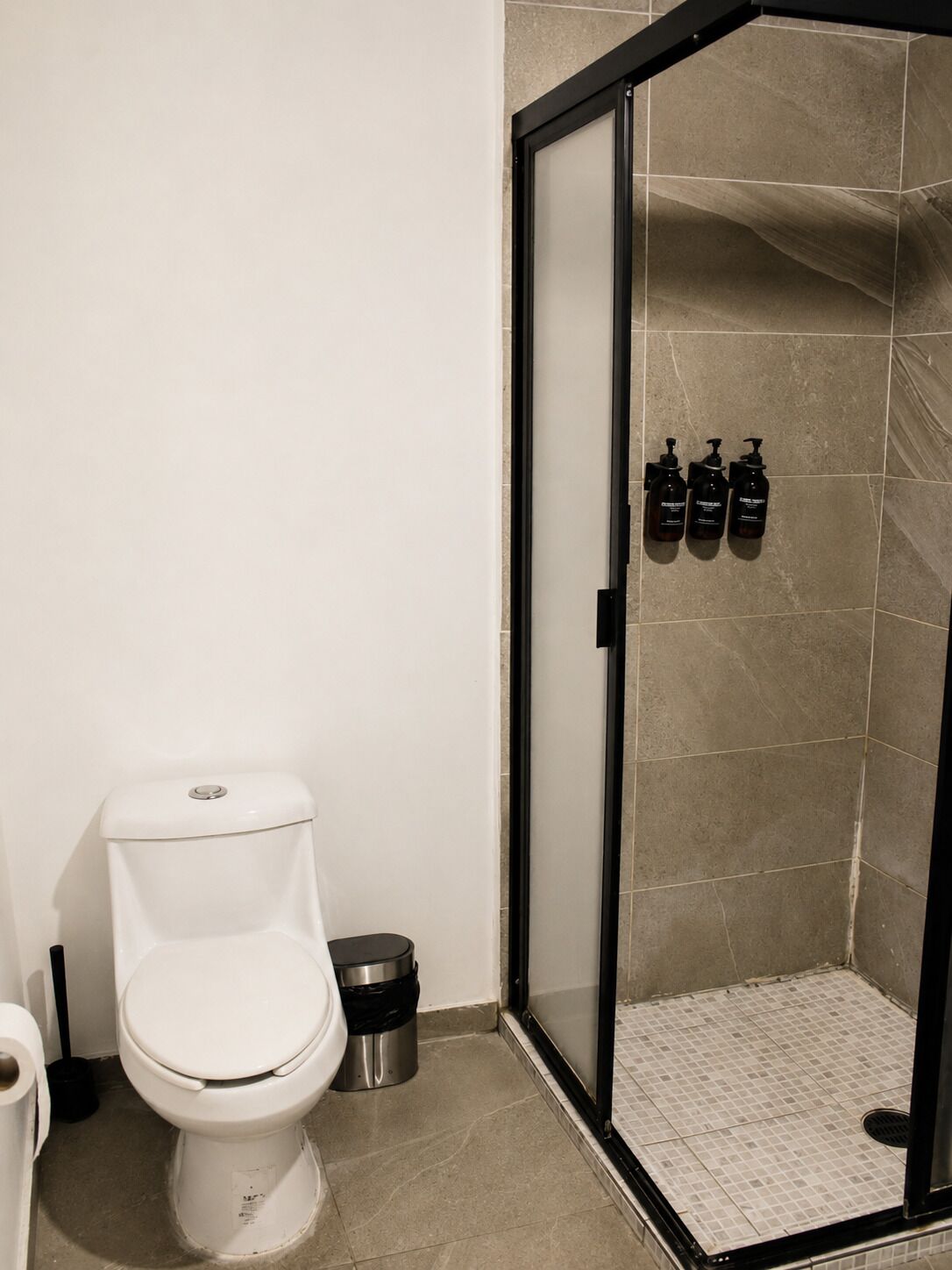 A bathroom with a toilet, a trash bin, and a shower area with a glass door.