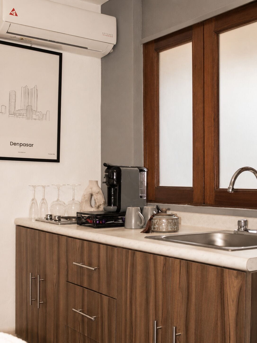 A kitchen with a coffee maker, wine glasses, and a framed cityscape.