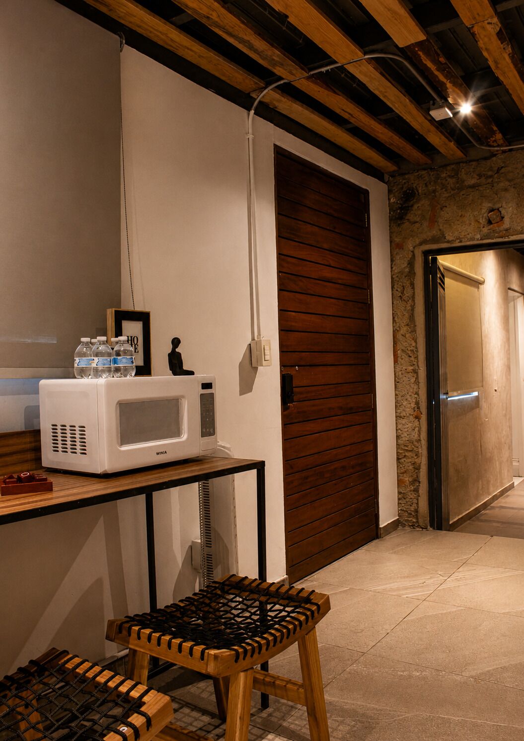 Una cocina con microondas, dispensador de agua y un taburete de madera.