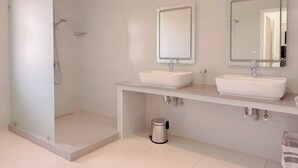 Een moderne badkamer met een douchecabine van glas, twee wastafels en spiegels boven elke wastafel.
