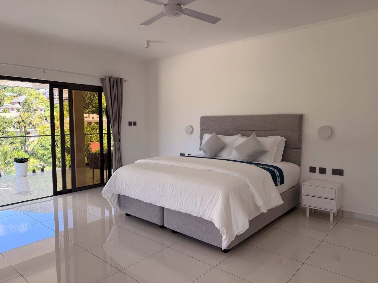 A bedroom with a bed, a nightstand, a ceiling fan, and a view through a glass door.
