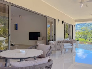 A modern living room with a flat-screen TV, a round dining table, and a sofa. - Cove Holiday Apartments (Bel Ombre)