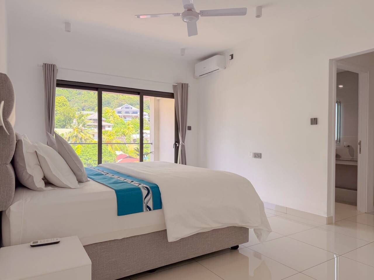 Ein modernes Hotelzimmer mit einem großen Bett, einem Deckenventilator, einer Klimaanlage und Blick auf Grünflächen.