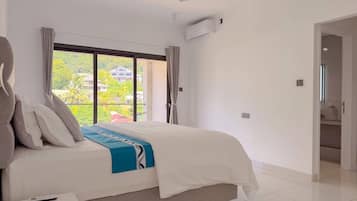 Ein modernes Hotelzimmer mit einem großen Bett, einem Deckenventilator, einer Klimaanlage und Blick auf Grünflächen.