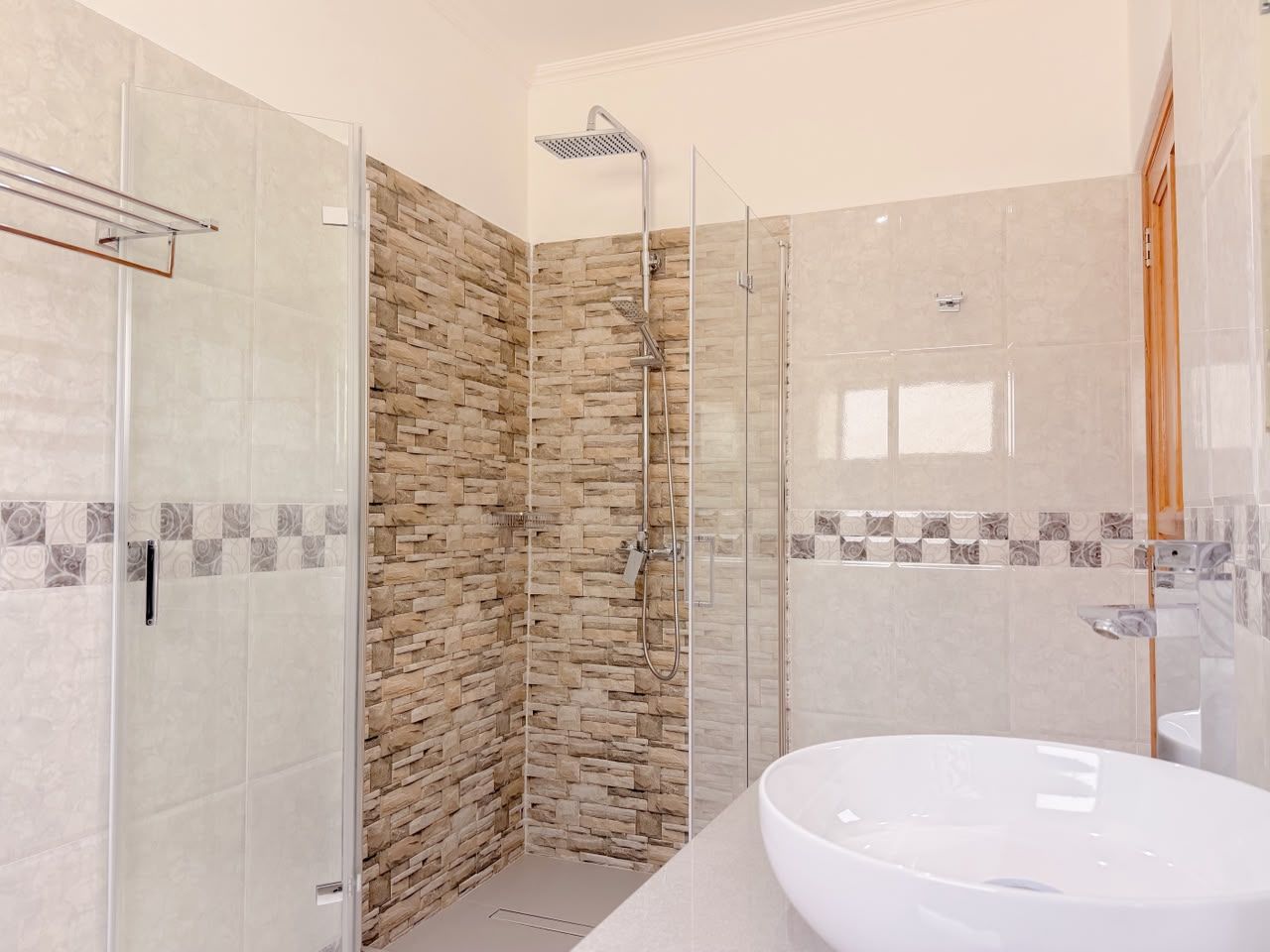 Un bagno moderno con box doccia in vetro, parete dalla texture simile alla pietra e un ampio lavandino bianco.