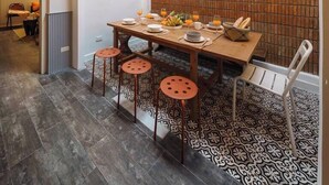 Un espace repas avec une table haute, des tabourets et un mur en briques en arrière-plan.