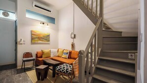Un salon avec un canapé, des fauteuils, une table basse, un escalier et un tableau accroché au mur.