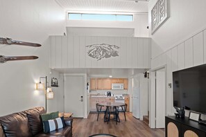 Ein modernes Interieur mit Essbereich, Küche und einem Schlafbereich im Zwischengeschoss mit Bergmotiv an der Wand.