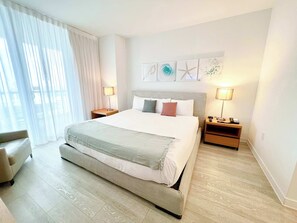 Een hotelkamer met een groot bed, twee nachtkastjes met lampen, een stoel en uitzicht op het landschap.