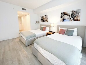 Habitación de hotel con dos camas, una mesita de noche, una lámpara y una obra de arte en la pared.