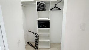 Ein weißer Kleiderschrank mit Regalen, einer Kleiderstange und einem schwarzen elektronischen Gerät.