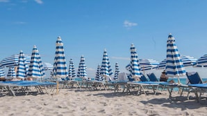 Ein Strand mit gestreiften Sonnenschirmen und Liegestühlen.