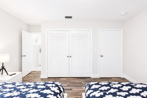 Ein Schlafzimmer mit zwei Betten, weißen Schränken, einem Nachttisch, einer Lampe und Holzboden.