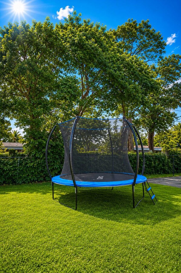Un trampoline doté d’un filet de sécurité, entouré d’herbe et d’arbres.