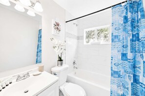 Ein modernes Badezimmer mit einem weißen Waschbecken, einer Toilette und einer Badewanne. Ein blauer Duschvorhang mit Fischmuster.