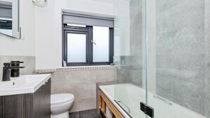 Un baño moderno con cabina de ducha de vidrio, inodoro blanco y tocador con lavamanos.