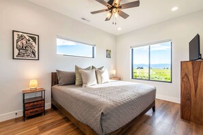 A bedroom with a bed, bedside tables, a ceiling fan, large windows, and artwork on the wall. - Upper-Level Living, Stars, HotTub, Mtn Views, Pets (Driggs)