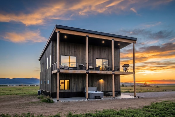 A modern two-story building with a balcony, outdoor seating, and a hot tub. - Upper-Level Living, Stars, HotTub, Mtn Views, Pets (Driggs)