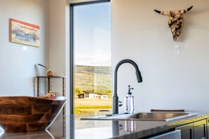 A modern kitchen with a large window, a bull skull decoration, and a wooden bowl on the counter. - Upper-Level Living, Stars, HotTub, Mtn Views, Pets (Driggs)