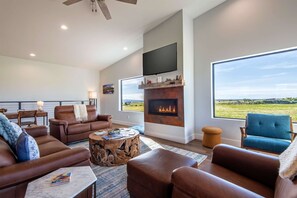 A spacious living room with leather sofas, a fireplace, a television, and a large window offering a view of the outdoors. - Upper-Level Living, Stars, HotTub, Mtn Views, Pets (Driggs)