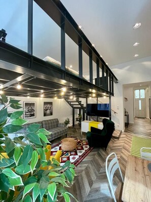 A modern living room with a high ceiling, a staircase, and a dining area. - Awesome Loft- King Street Budapest (Budapest)