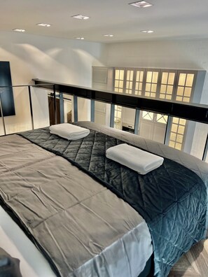A modern hotel room with a large bed, a balcony with a glass railing, and a view of the outside.