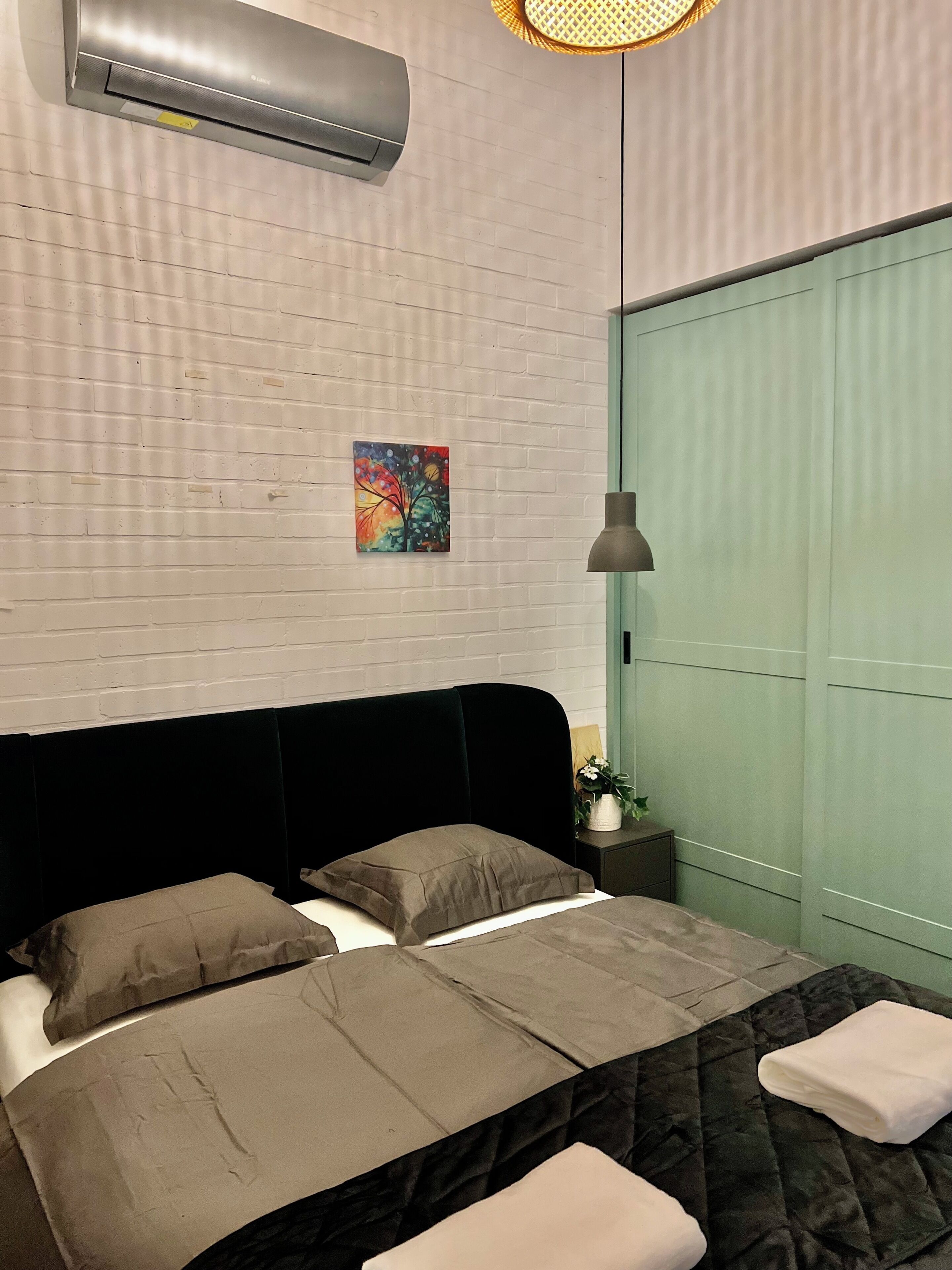 A bedroom with a bed, a nightstand, a wall-mounted air conditioner, a painting, and a green door.