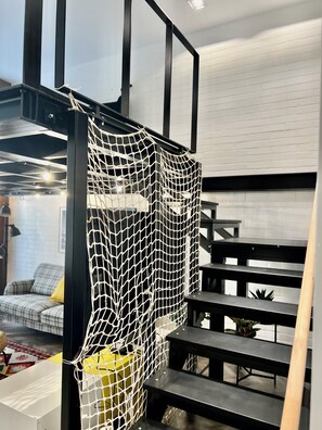 A modern interior with a staircase, a netted partition, and a sofa with a yellow cushion.