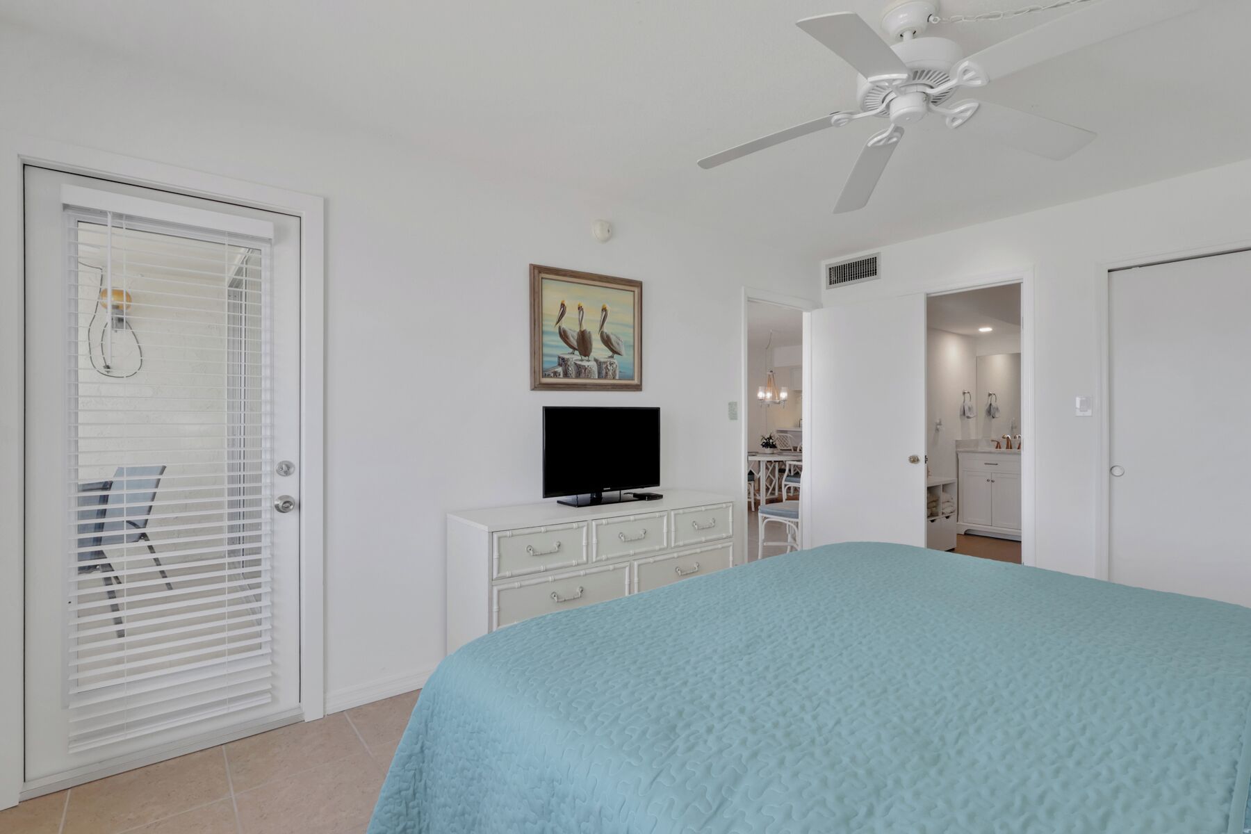 A bedroom with a bed, a television, a ceiling fan, and a painting.