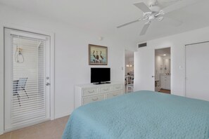 Quarto com uma cama, televisão, ventilador de teto e um quadro.