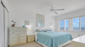 A bedroom with a bed, a dresser, a nightstand, a ceiling fan, a map on the wall, and a window with a view of the sea. - Gulf-Front Bonita Beach, FL Condo -  Private Beach Access + Pool / Gulf views (Bonita Springs)
