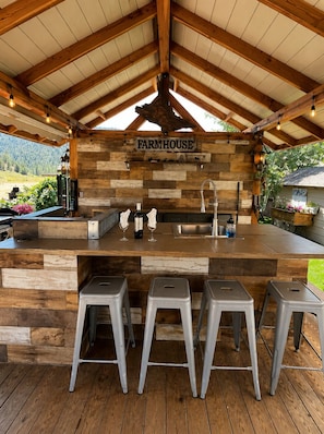 A rustic farmhouse bar with wooden walls, a metal countertop, and three metal stools.