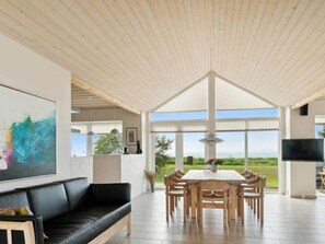 Uma sala de estar ampla com um sofá de couro preto, uma mesa de jantar com cadeiras de madeira, um quadro abstrato grande e uma televisão.