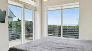 A bedroom with a large bed, sliding glass doors to a balcony, and a ceiling light fixture. - 4 Star Holiday Home in Ebeltoft (Ebeltoft)
