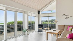 A spacious living area with large windows, a sofa, a coffee table, and a chair. - 4 Star Holiday Home in Ebeltoft (Ebeltoft)