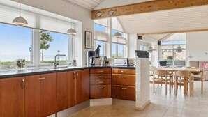 A modern kitchen with wooden cabinets, a dining area with a table and chairs, and large windows offering a view. - 4 Star Holiday Home in Ebeltoft (Ebeltoft)